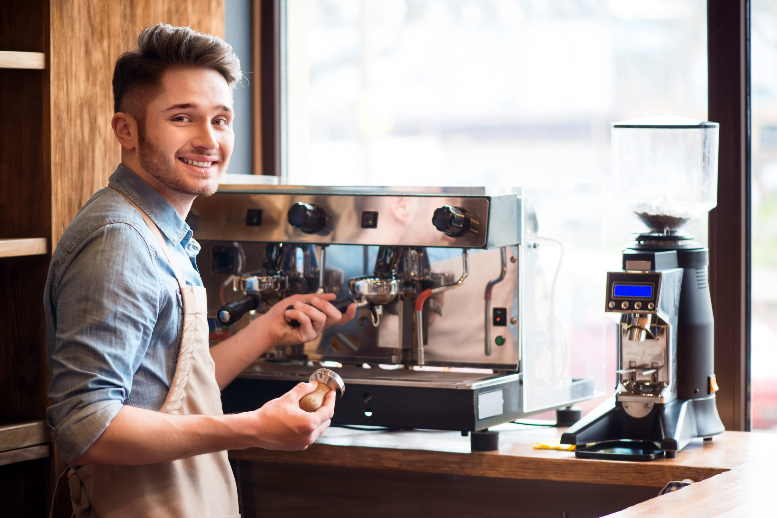 An enthusiastic barista smiling for the photo as he works the coffee machine.