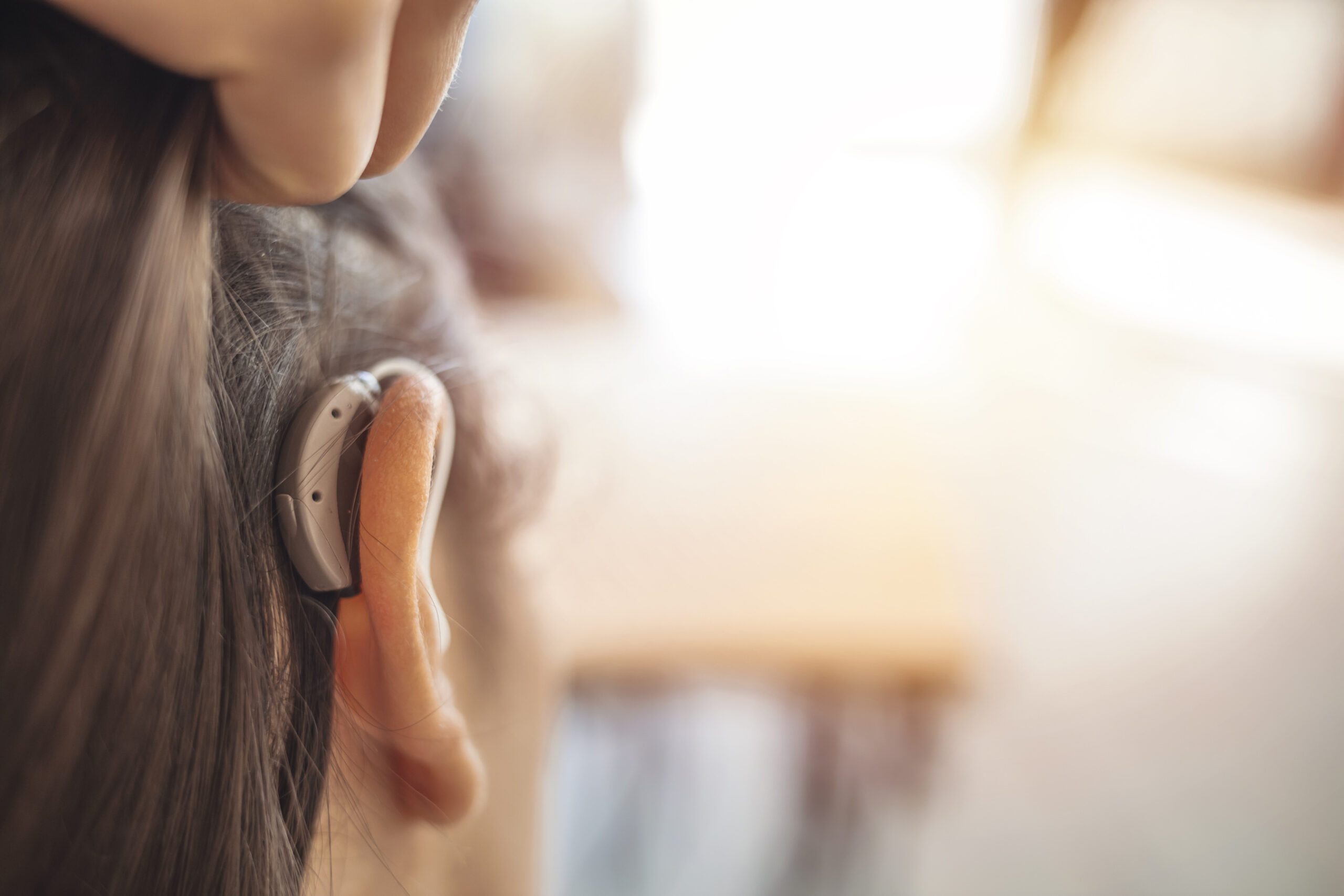 A woman pushes her hair back to put focus on a hearing aid in her ear.