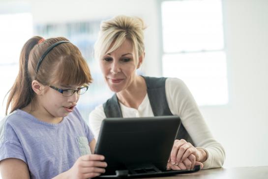 A girl with glasses is looking and doing something on her computer and a woman is sitting right next to her.